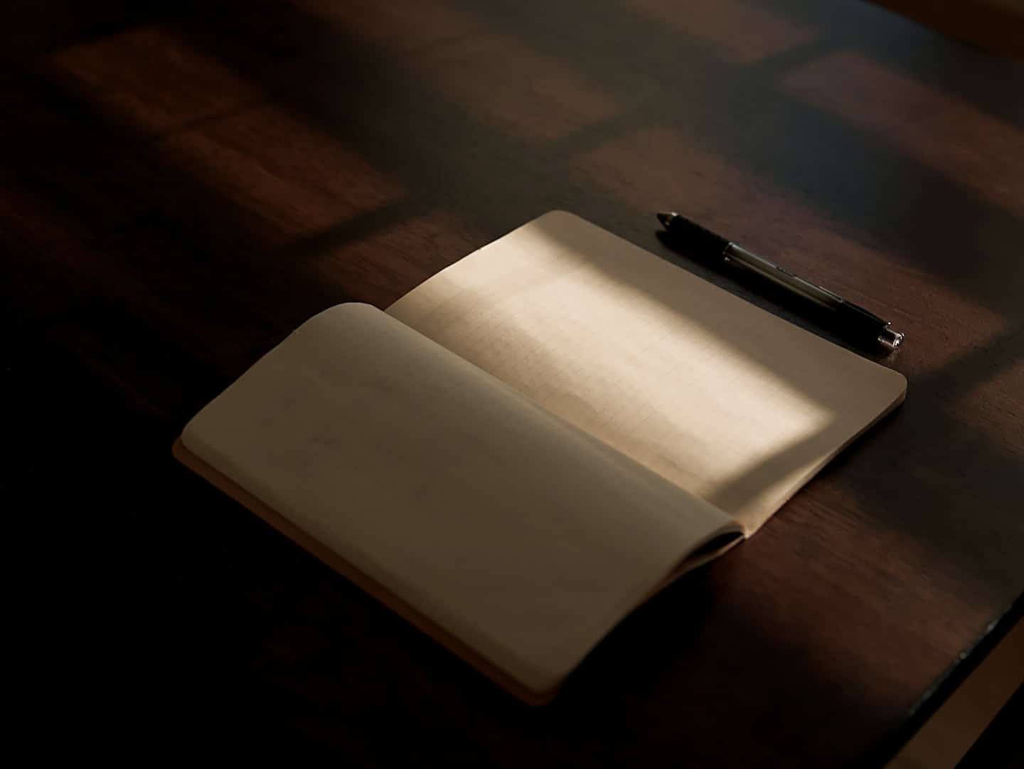 An open notebook and pen on a wooden desk.